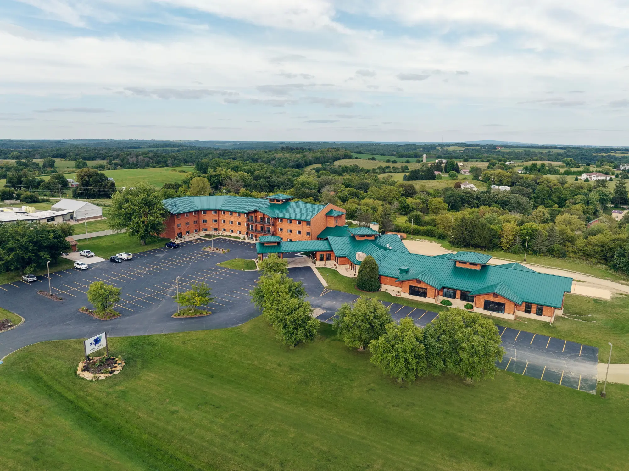 Aerial view of the Wood Violet Recovery Center surrounded by greenery, showing the full facility and parking lot.