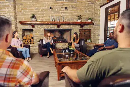 A group of individuals engaging in a counseling session at Wood Violet Recovery, seated around a coffee table in a cozy room with a fireplace in the background.