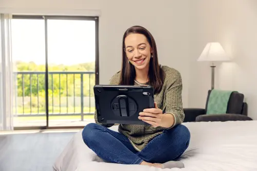 Woman using a tablet while sitting on a bed at Wood Violet Recovery.