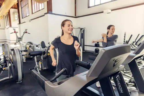 Two women exercising on treadmills at the fitness center in Wood Violet Recovery.